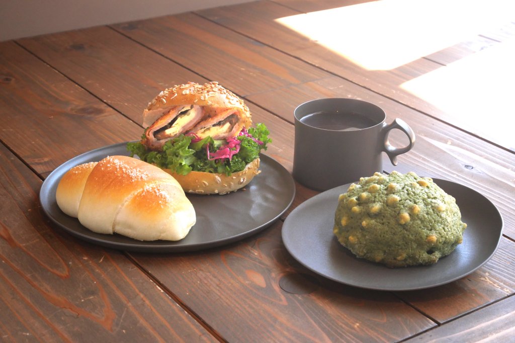 左から、「塩パン」（190円）、「NONOJI BURGER（梅しそチーズ）」（480円）、「アメリカーノ」（550円）、「抹茶メロンパン」（280円）。ドリンクはパンを2点以上購入すると100円引きに。